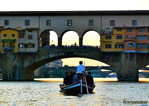 A traditional Florentine boat, called 'barchetto', goes under the Ponte Vecchio at dusk